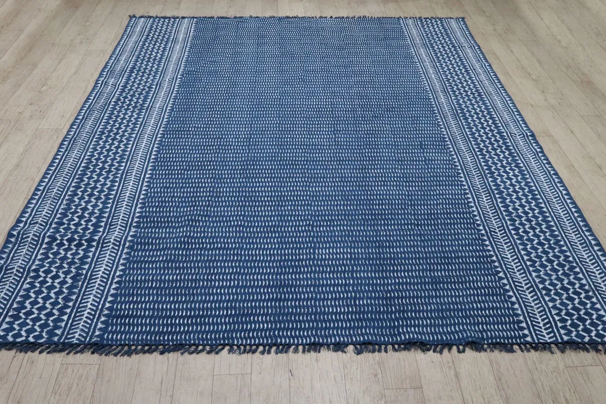 A rectangular flatwoven rug in deep indigo blue with cream chevron-patterned borders, laid flat on a light wood floor.