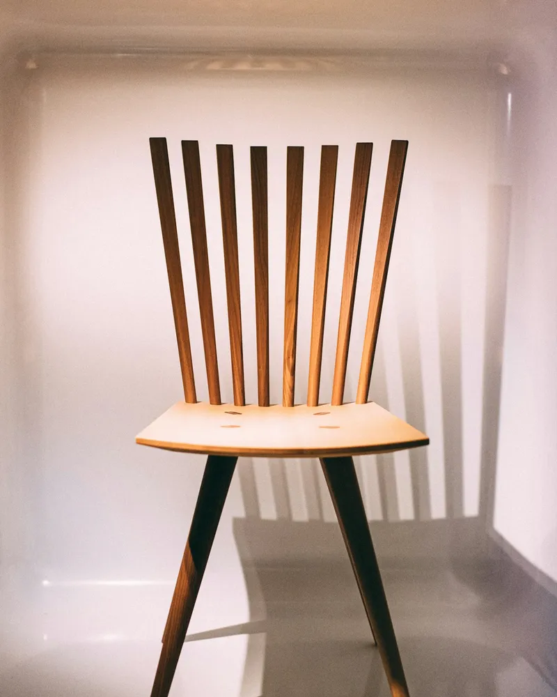 Walnut dining chair with a comb-back of eight tapered vertical wood spindles rising from a shaped plywood seat, on splayed legs, against a plain neutral background.