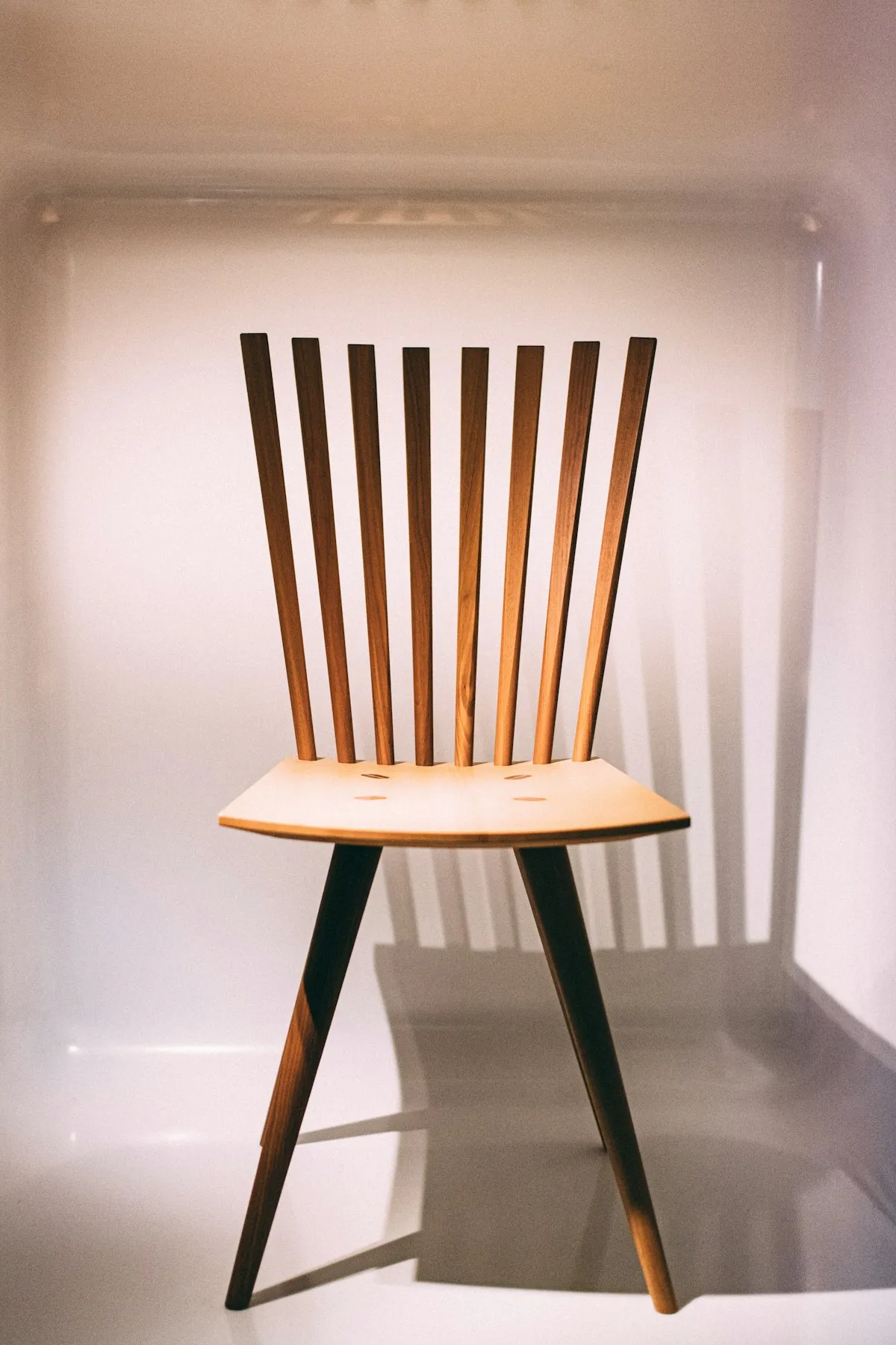 Walnut dining chair with a comb-back of eight tapered vertical wood spindles rising from a shaped plywood seat, on splayed legs, against a plain neutral background.