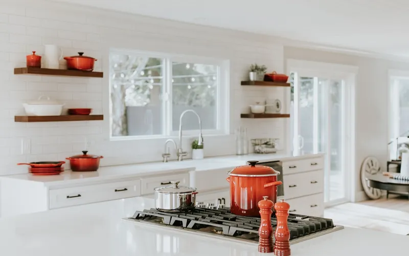 White kitchen with open wood shelving, marble counters, and warm-toned cookware accents