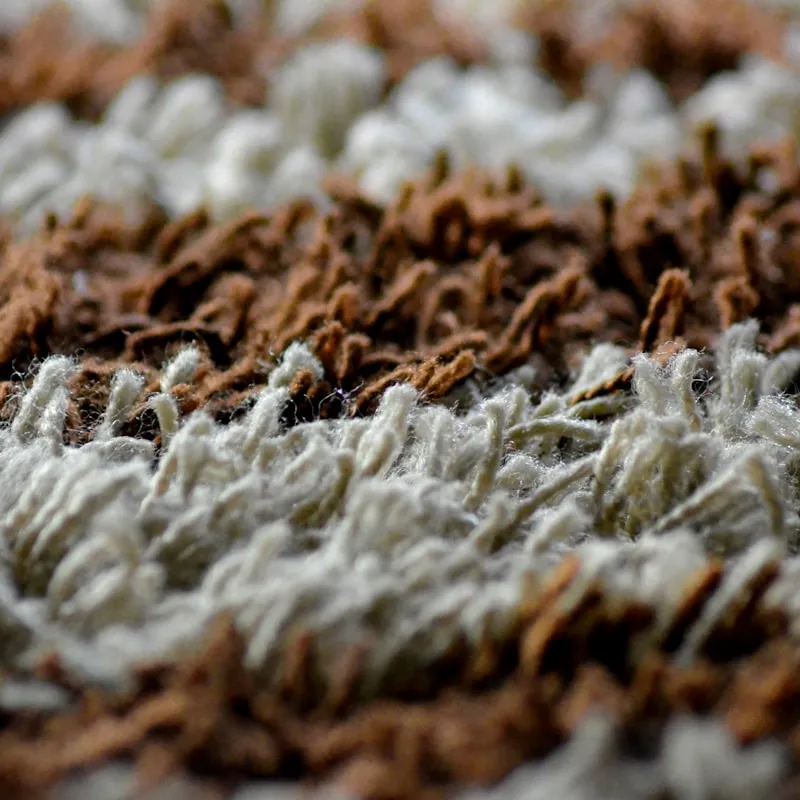 Extreme close-up of a shag wool rug's pile, showing rows of cream and brown wool tufts in alternating bands of texture.