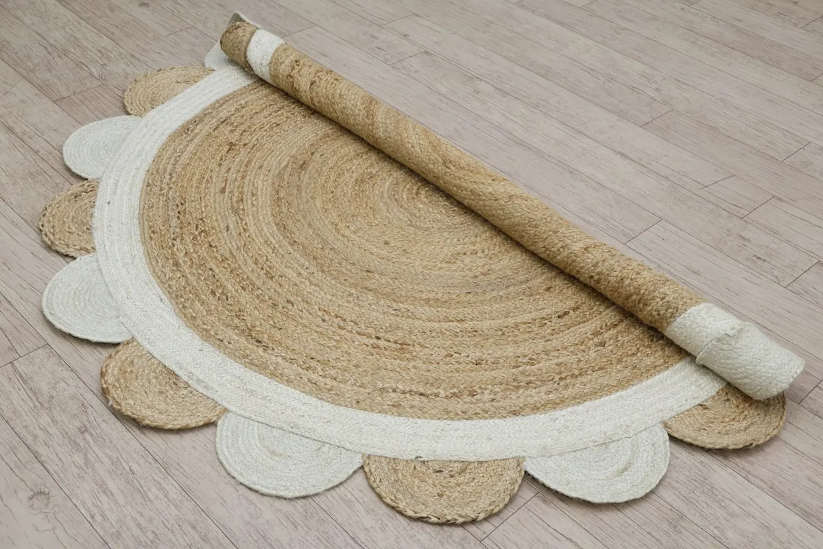 A half-rolled circular jute rug with a scalloped cream cotton border, shown partially unrolled on a light wood floor.