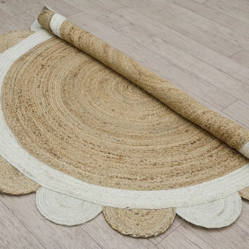 A half-rolled circular jute rug with a scalloped cream cotton border, shown partially unrolled on a light wood floor.