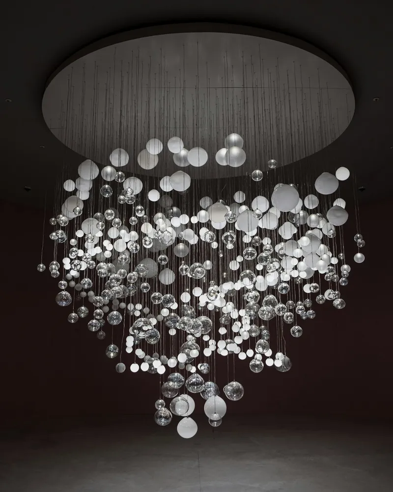 A large chandelier made of dozens of clear and frosted glass spheres of varying sizes, suspended from a round ceiling canopy in a dark room.