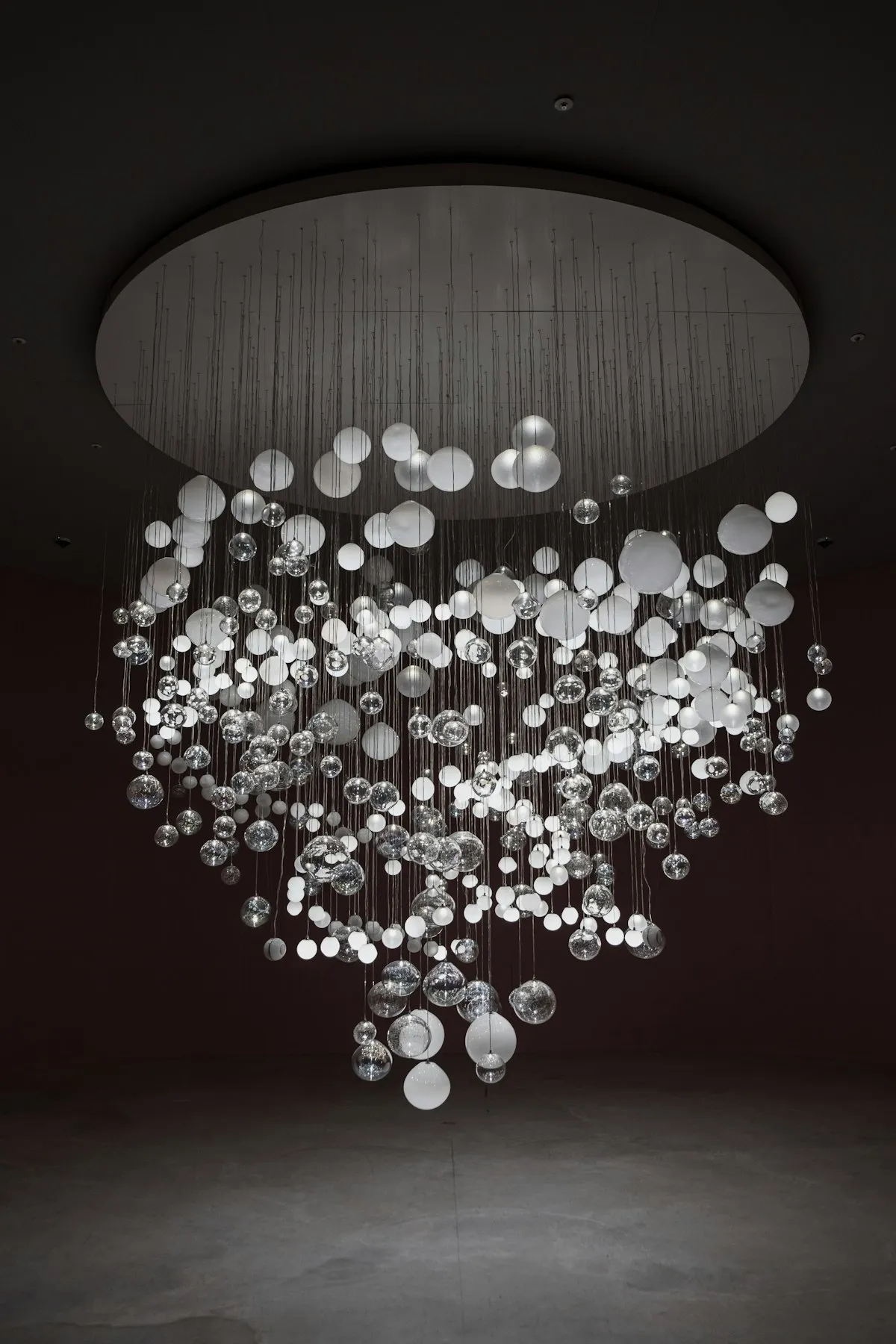 A large chandelier made of dozens of clear and frosted glass spheres of varying sizes, suspended from a round ceiling canopy in a dark room.