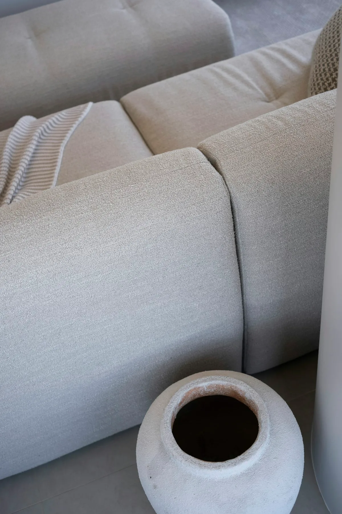 Close-up detail of a beige bouclé modular sofa showing the seam where two individual seat modules meet, with a striped throw and a ceramic vase in the foreground.