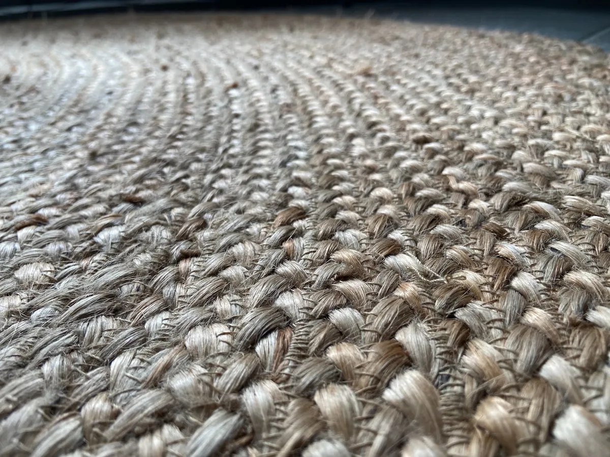 Low-angle close-up of a braided jute rug's edge, showing the coiled rope construction and natural fibre texture.