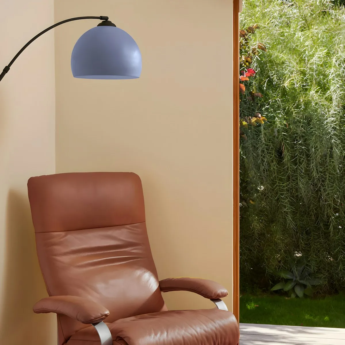 A blue-grey dome-shaded arc floor lamp curving over a brown leather armchair near a sunlit garden doorway.