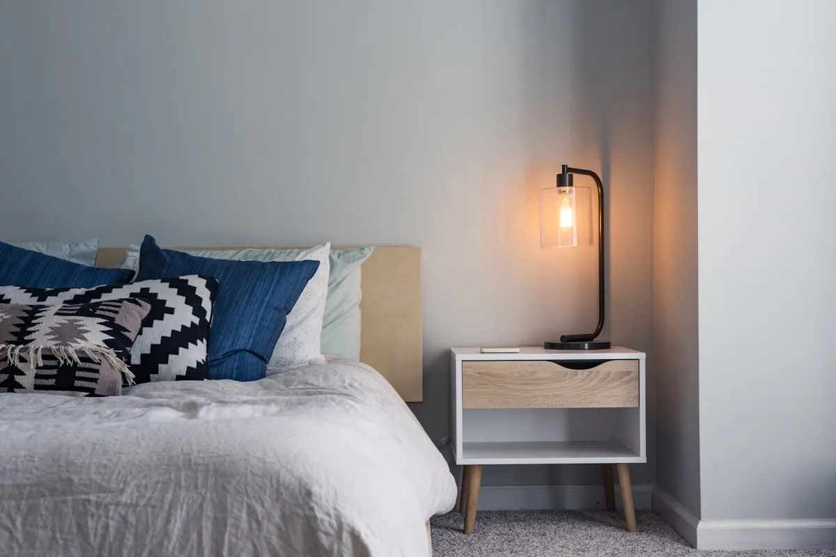 Light oak nightstand with a black table lamp beside a linen-covered bed