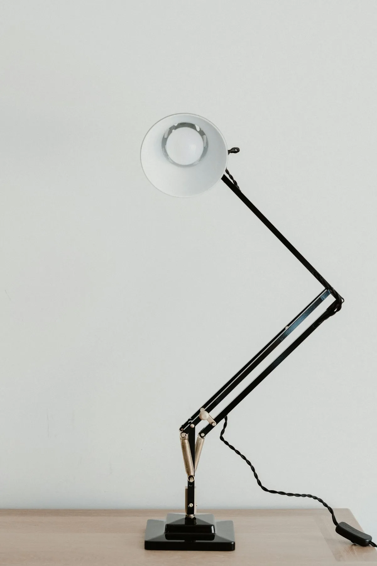 A black articulated task lamp with a swing arm and cone-shaped shade, photographed against a plain white wall.