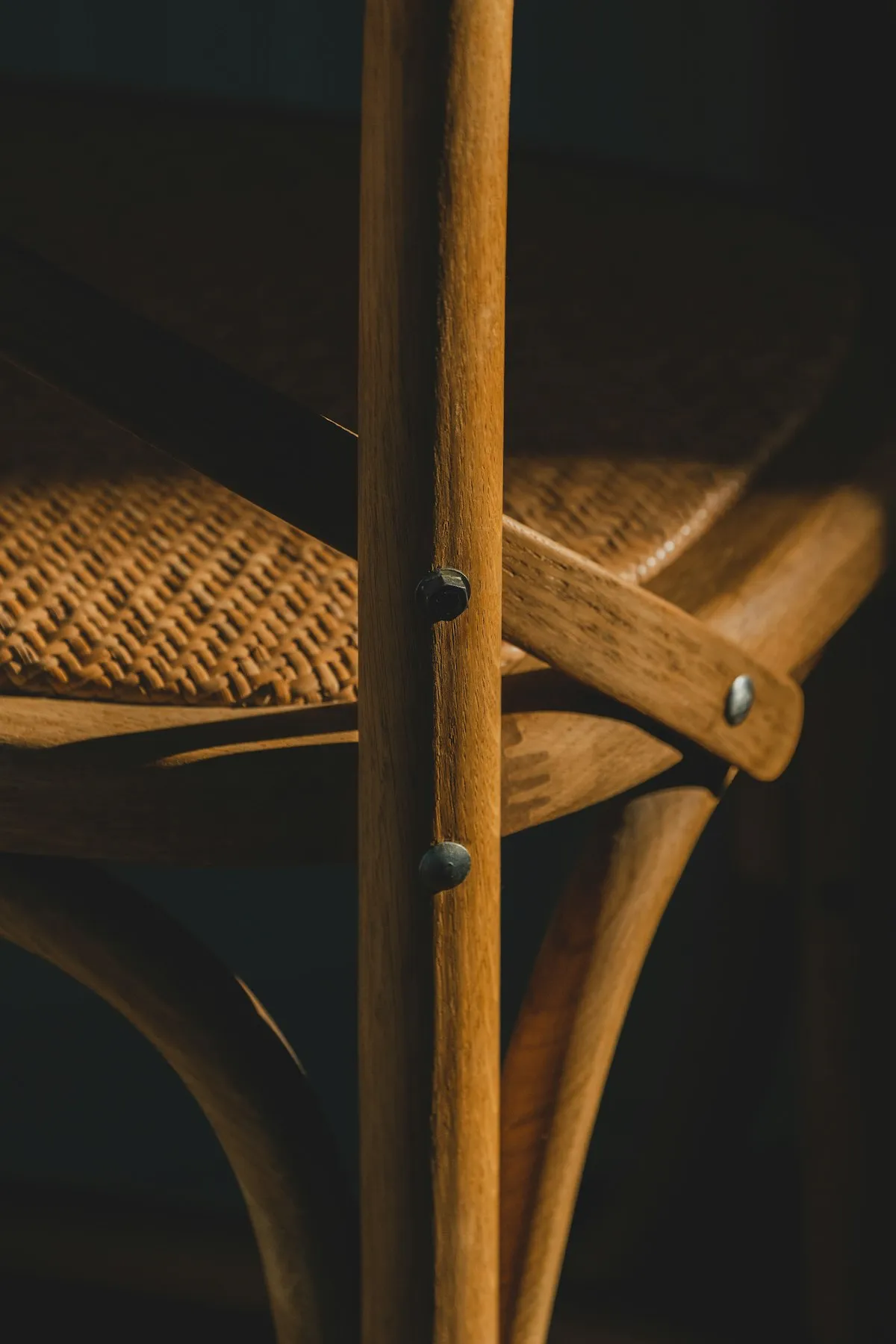 Close-up detail of a woven cane chair seat and backrest joint, showing the hand-woven basketry pattern secured to the dark wood frame with visible screws.