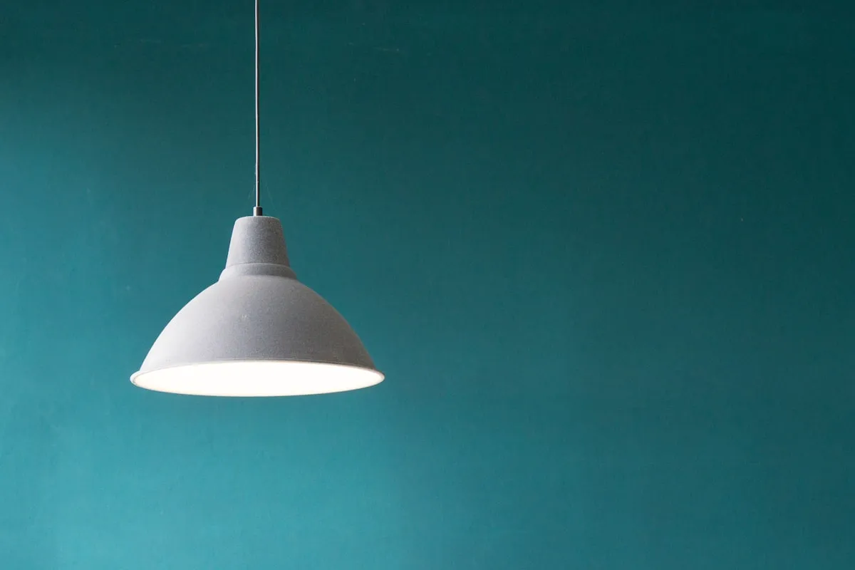 A matte grey dome pendant light hanging against a solid dark teal wall, illuminated from within.
