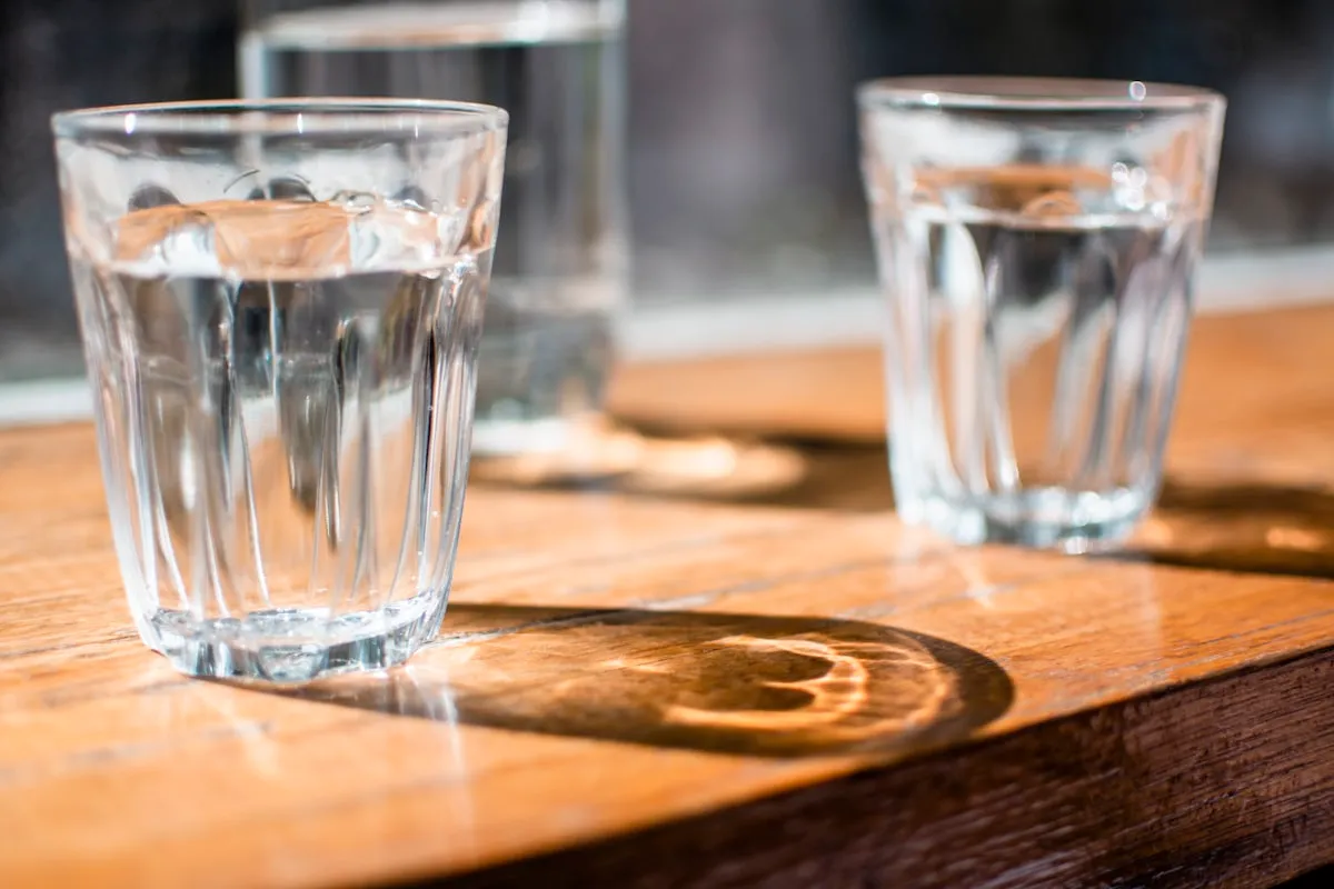 Three clear faceted drinking glasses filled with water on a wooden table, warm side light casting reflections.
