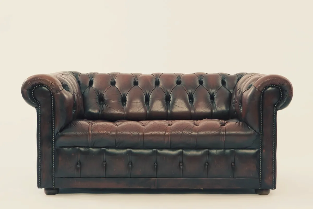Dark brown tufted leather Chesterfield-style two-seat sofa with rolled arms and nailhead trim, on a plain neutral background.