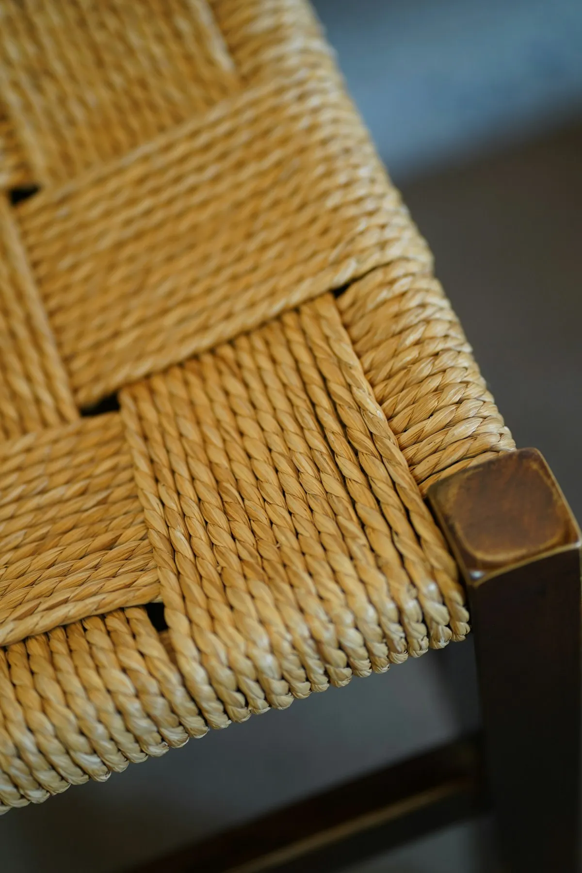 Macro detail of a woven seagrass cord dining chair seat, showing the crosshatch weave pattern meeting the dark wood corner post.