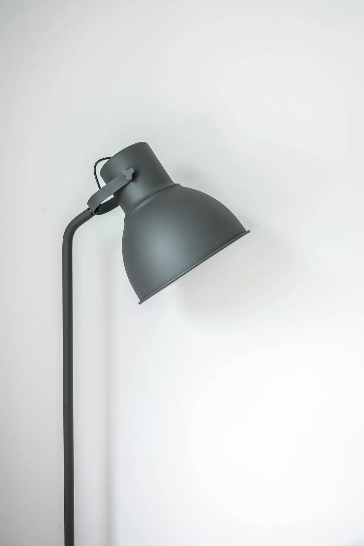 A matte grey adjustable floor lamp with an angled cone shade, photographed against a plain white wall.