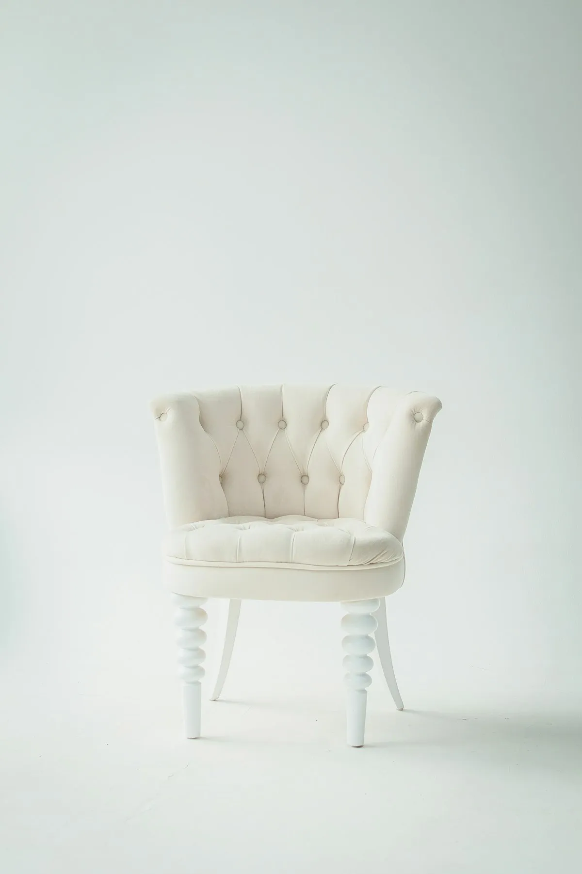 Cream tufted velvet armchair with a button-diamond backrest and turned bobbin-style white-lacquered legs, on a plain white background.
