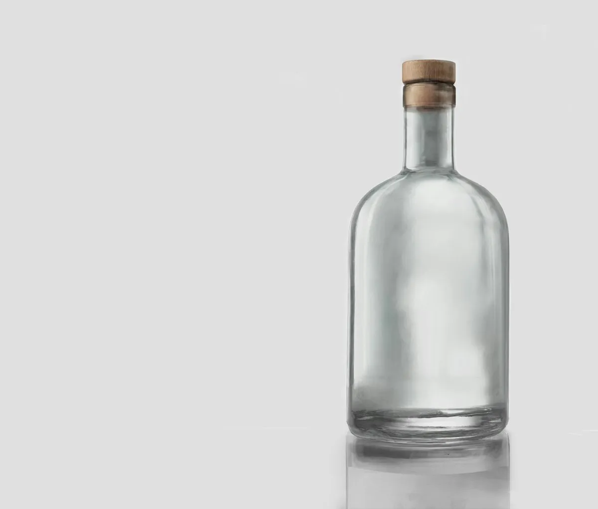 Clear glass bottle with a rounded shoulder and a wood-and-cork stopper, on a plain light grey studio background.