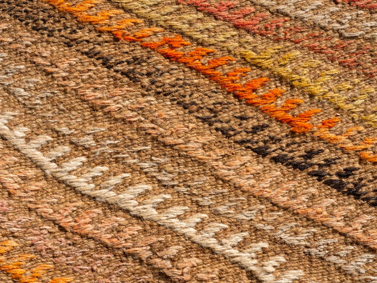 Close-up of a hand-woven kilim-style rug surface showing an orange, yellow, black, and cream diagonal chevron pattern.